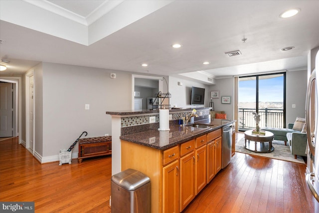 kitchen with sink, crown molding, dark stone counters, and a center island with sink