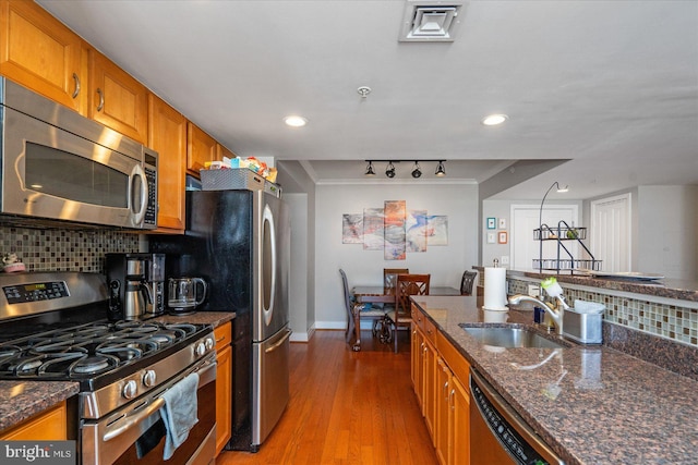 kitchen featuring sink, dark stone countertops, backsplash, light hardwood / wood-style floors, and stainless steel appliances