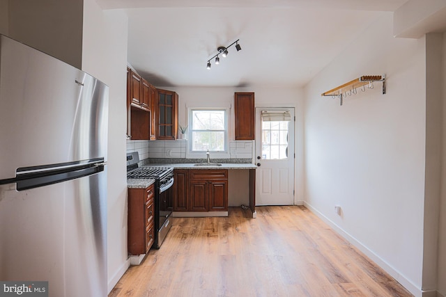 kitchen featuring stainless steel appliances, decorative backsplash, dark stone counters, light hardwood / wood-style flooring, and sink