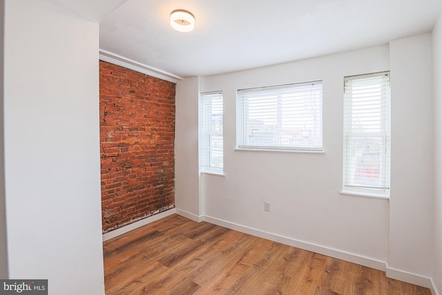 unfurnished room with a wealth of natural light, brick wall, and hardwood / wood-style flooring