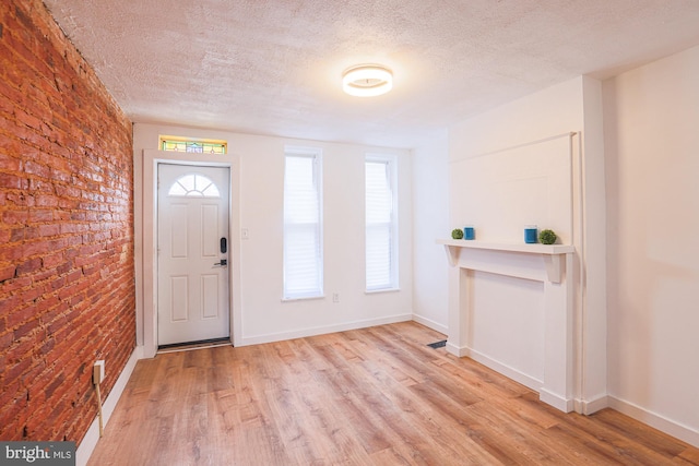 foyer entrance with plenty of natural light, brick wall, a textured ceiling, and light hardwood / wood-style flooring