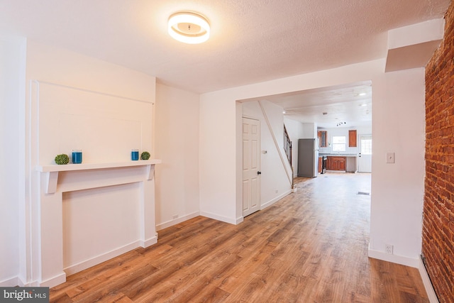 corridor featuring brick wall, a textured ceiling, and hardwood / wood-style floors