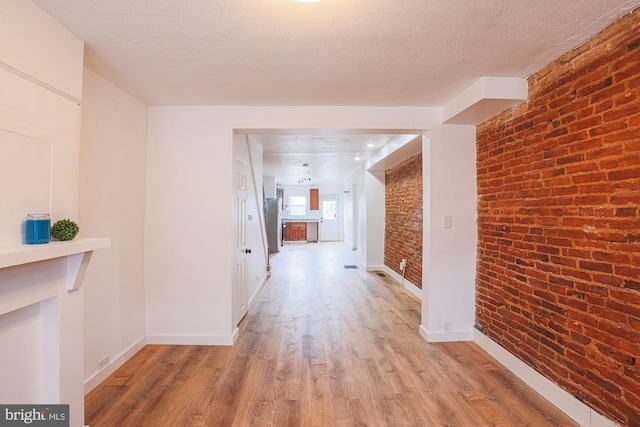 corridor with brick wall, a textured ceiling, and light wood-type flooring