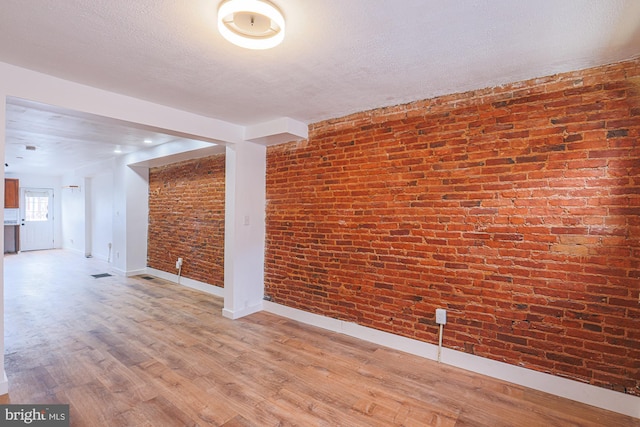 unfurnished room with brick wall, a textured ceiling, and hardwood / wood-style floors