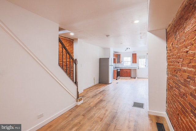 corridor with brick wall, light hardwood / wood-style floors, and sink