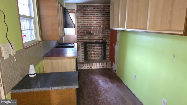 kitchen featuring backsplash, a brick fireplace, light brown cabinetry, dark hardwood / wood-style flooring, and gas cooktop