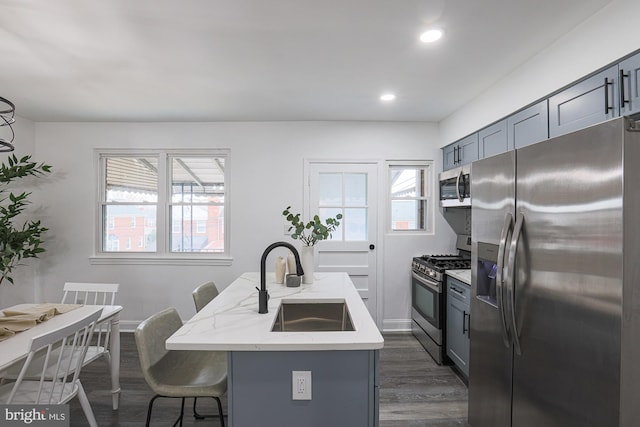 kitchen featuring dark wood-style floors, light stone countertops, an island with sink, a sink, and stainless steel appliances