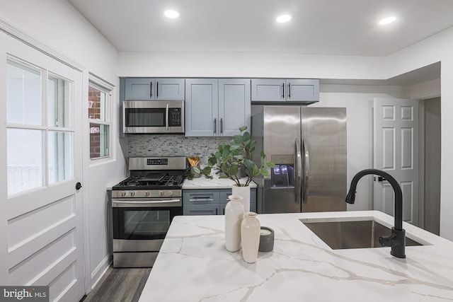 kitchen with a sink, light stone counters, tasteful backsplash, dark wood finished floors, and appliances with stainless steel finishes