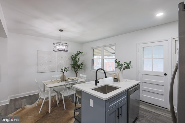 kitchen with dark wood finished floors, a kitchen island with sink, a sink, dishwasher, and a notable chandelier