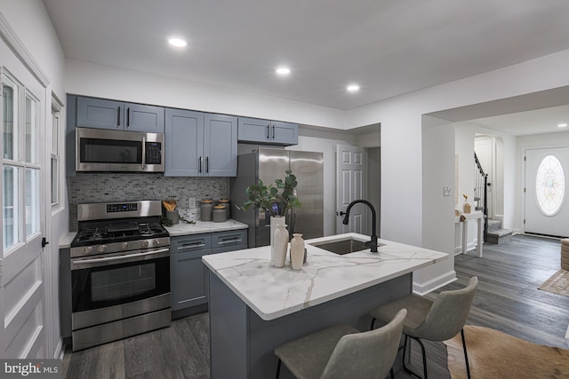 kitchen with gray cabinets, a sink, appliances with stainless steel finishes, light stone countertops, and dark wood-style flooring