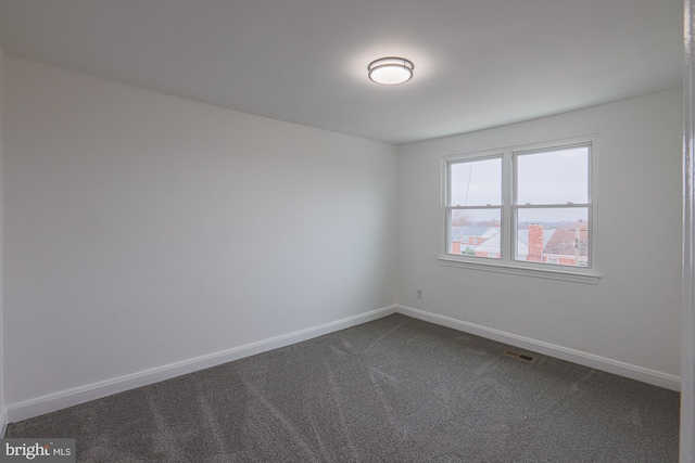 empty room featuring visible vents, dark carpet, and baseboards