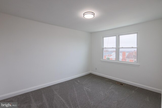 spare room featuring visible vents, baseboards, and dark carpet