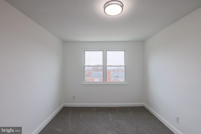 spare room featuring visible vents, baseboards, and dark colored carpet