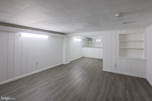 basement featuring built in features, visible vents, dark wood-style flooring, and baseboards