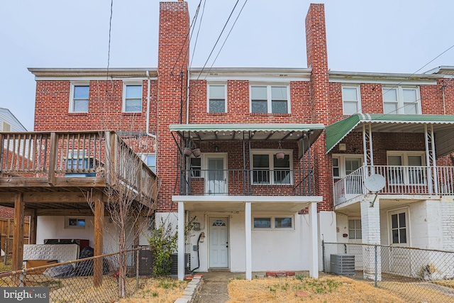 view of front facade featuring brick siding, central AC unit, a chimney, and fence