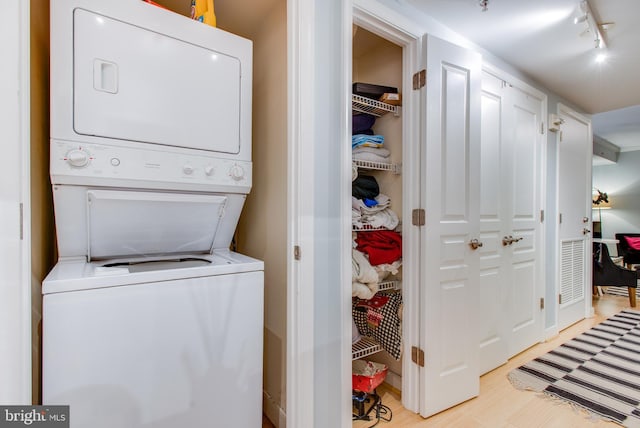 laundry area with rail lighting, light hardwood / wood-style flooring, and stacked washer and clothes dryer