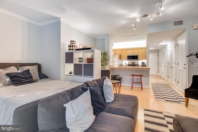 bedroom with light hardwood / wood-style floors, ornamental molding, rail lighting, and stainless steel refrigerator