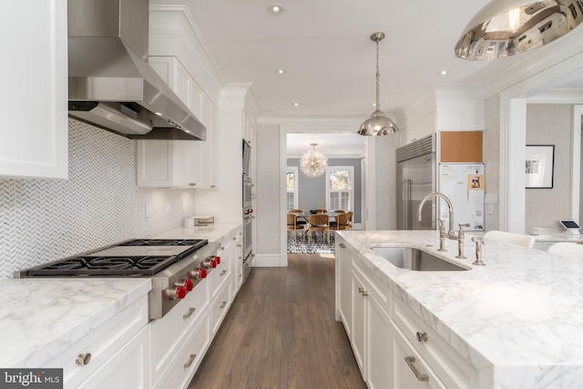 kitchen with ornamental molding, appliances with stainless steel finishes, an inviting chandelier, wall chimney exhaust hood, and a sink