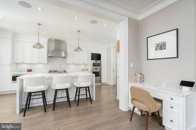 kitchen featuring a kitchen breakfast bar, white cabinetry, crown molding, and wall chimney range hood