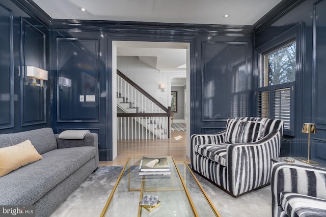 living area with a decorative wall, wood finished floors, stairs, and crown molding