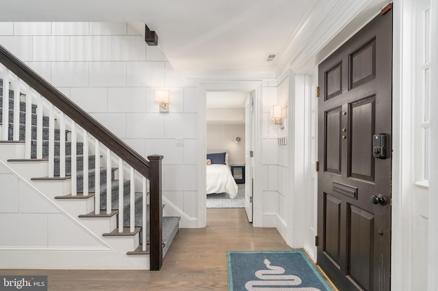 entryway featuring stairway, wood finished floors, visible vents, and ornamental molding