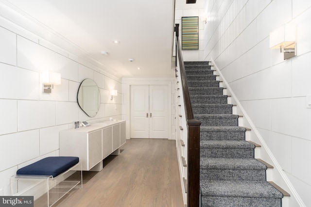 staircase featuring recessed lighting, tile walls, wood finished floors, and crown molding