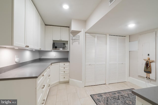 kitchen with white cabinetry, stainless steel microwave, dark countertops, and visible vents