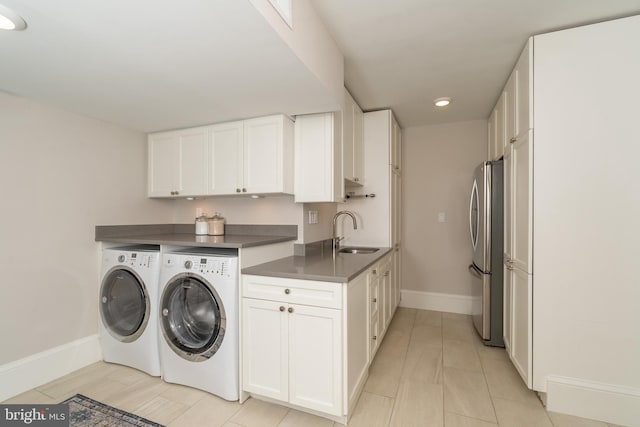 clothes washing area featuring washing machine and clothes dryer, cabinet space, baseboards, and a sink