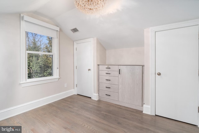 additional living space with wood finished floors, visible vents, baseboards, an inviting chandelier, and vaulted ceiling