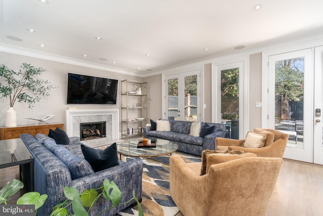 living room with light wood-type flooring, a fireplace, crown molding, and french doors