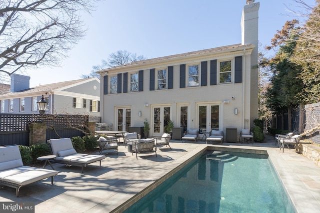 rear view of house with french doors, an outdoor pool, an outdoor hangout area, a chimney, and a patio area