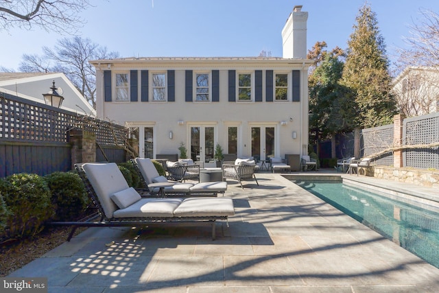 rear view of property featuring an outdoor living space, a patio, fence, french doors, and a chimney