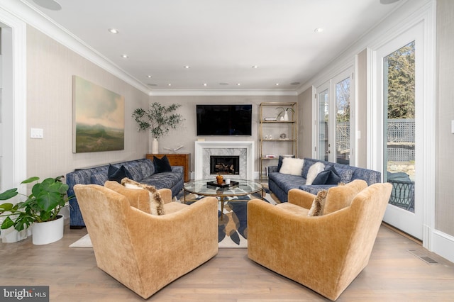 living area with visible vents, light wood-style floors, and a high end fireplace