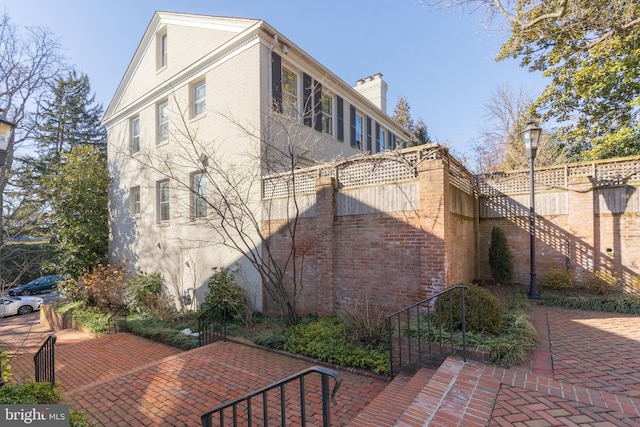 view of side of home with brick siding, fence, a chimney, and a patio area