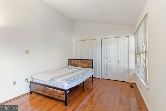 bedroom with hardwood / wood-style flooring, lofted ceiling, and two closets