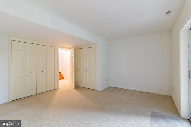 unfurnished bedroom with light colored carpet and multiple closets