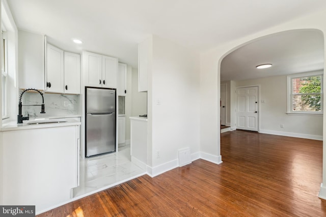 kitchen featuring hardwood / wood-style floors, sink, tasteful backsplash, white cabinetry, and stainless steel refrigerator