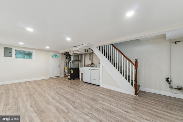 basement featuring electric panel, light hardwood / wood-style flooring, heating unit, and washing machine and clothes dryer