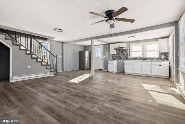 unfurnished living room with ceiling fan, wood-type flooring, sink, and a baseboard heating unit