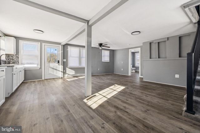 unfurnished living room featuring ceiling fan, beam ceiling, dark hardwood / wood-style flooring, and a baseboard heating unit