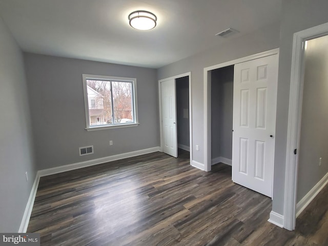 unfurnished bedroom featuring multiple closets and dark wood-type flooring