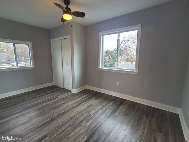 unfurnished bedroom featuring ceiling fan, a closet, dark hardwood / wood-style flooring, and multiple windows