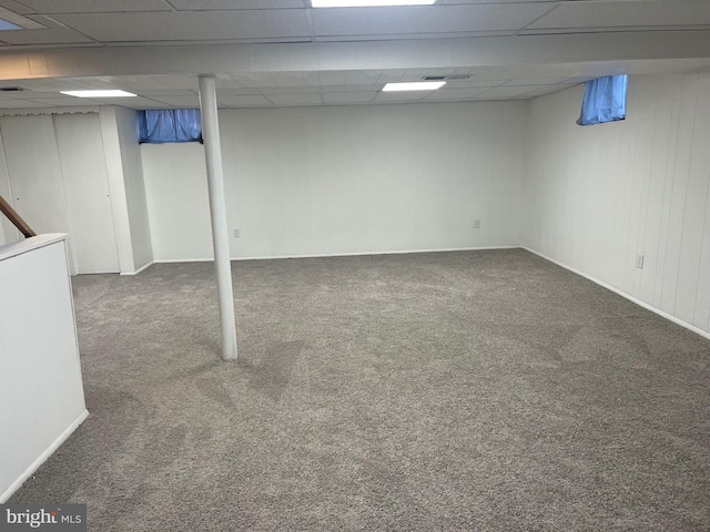 basement with a paneled ceiling and dark colored carpet