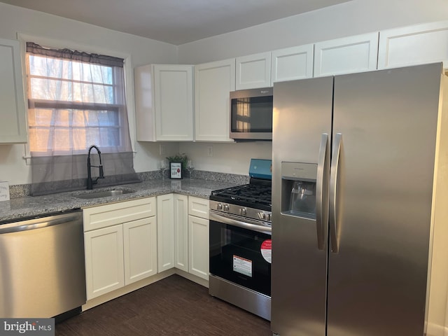 kitchen with light stone countertops, appliances with stainless steel finishes, white cabinetry, sink, and dark wood-type flooring