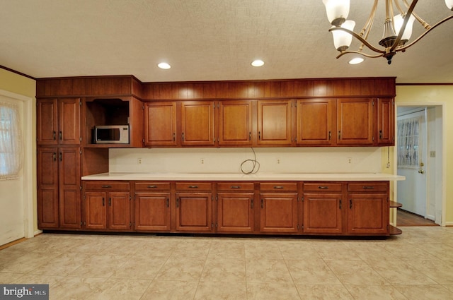 kitchen with decorative light fixtures, an inviting chandelier, built in microwave, and crown molding