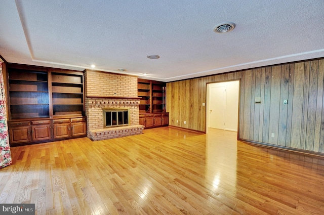 unfurnished living room featuring a textured ceiling, light hardwood / wood-style floors, a brick fireplace, and wooden walls