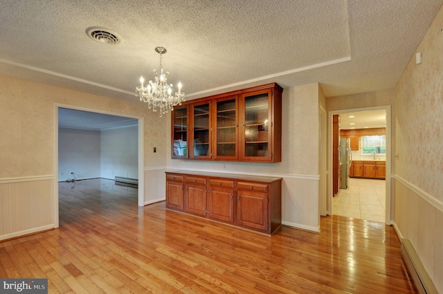 unfurnished dining area with a textured ceiling, light hardwood / wood-style floors, a baseboard radiator, and an inviting chandelier