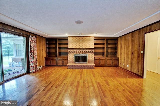 unfurnished living room with light wood-type flooring, a brick fireplace, built in shelves, a textured ceiling, and a baseboard heating unit