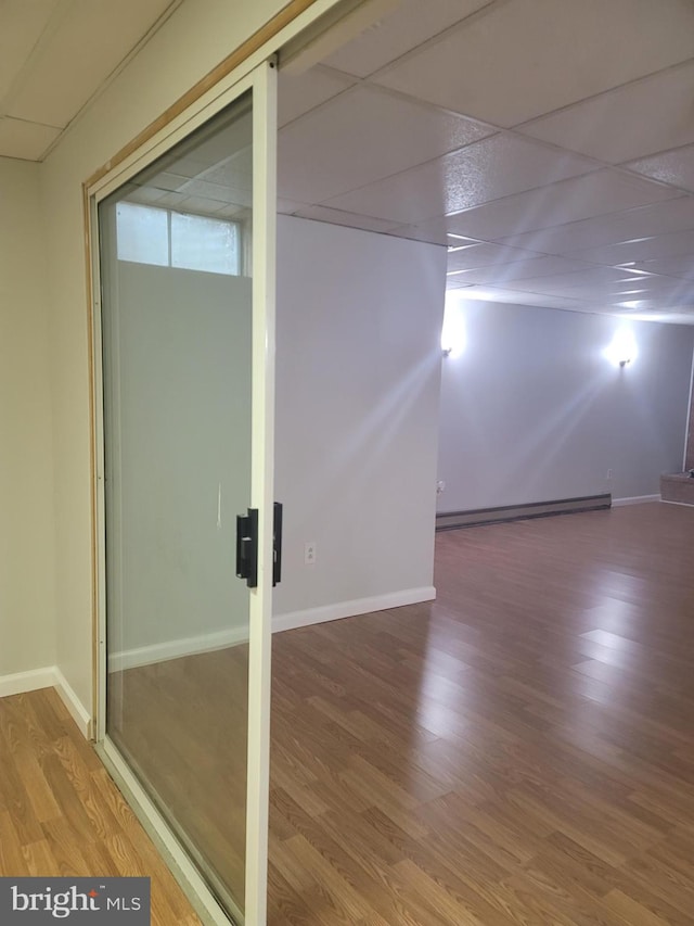 basement featuring hardwood / wood-style floors, a baseboard radiator, and a drop ceiling