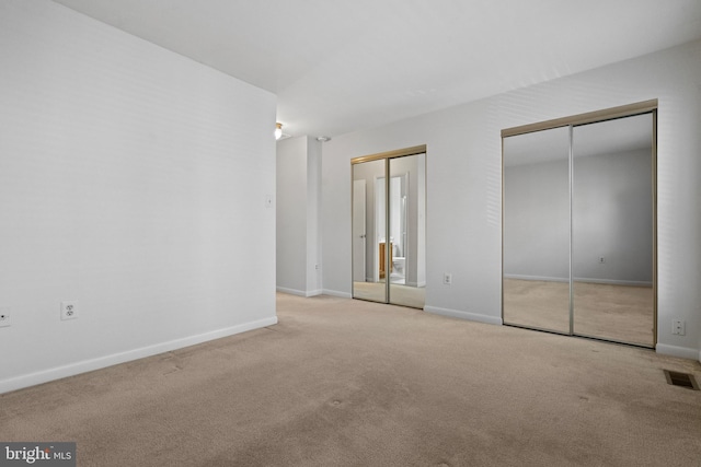 unfurnished bedroom with light carpet and multiple closets